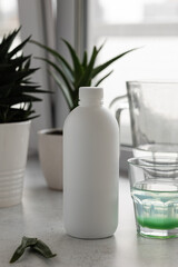 A white bottle with medicinal aloe juice on the background of a glass with juice diluted in water and an aloe flower. The concept of using natural plants in the treatment of stomach diseases.
