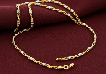 A twisted gold chain with silver accents rests against a maroon backdrop here