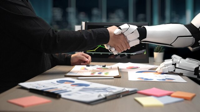 A human and a robotic arm engage in a handshake, symbolizing collaboration between technology and business in a modern office setting, reflecting innovation.Noogenesis