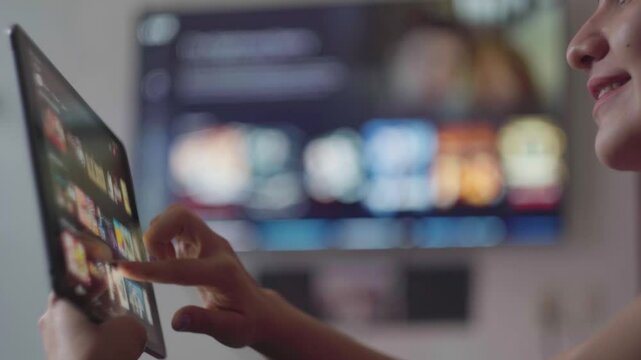 Woman browsing streaming service on tablet, selecting movie with smart tv nearby, relaxing in home living room during quiet evening