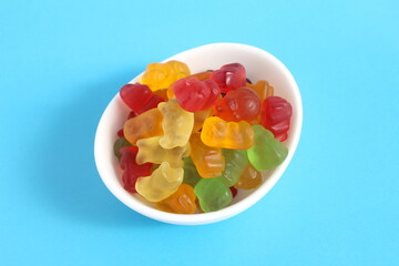 On a blue background there is a white bowl with multi-colored marmalade.	
