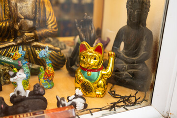 Lucky golden waving cat among colorful figurines and Buddha statues. Asian-inspired decoration,...