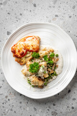 A gourmet dish featuring a baked chicken breast topped with melted cheese and tomato slices, accompanied by a creamy vegetable medley of peas, cauliflower, and potatoes, garnished with fresh parsley
