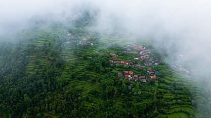 Aerial view of a misty mountain village with colorful houses nestled among lush green terraced fields.