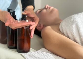 Young woman receiving a relaxing face and head  massage from a professional masseuse at a spa salon, lying on a massage table, with lotions 