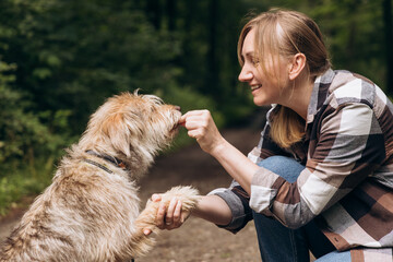Dog training session in a forest setting, woman engaging with her pet, showcasing positive reinforcement and bonding moments in nature