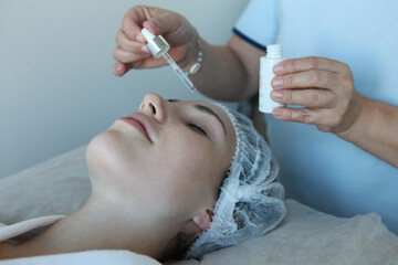 woman receiving a skincare treatment in a beauty spa or aesthetic clinic, with a beautician applying facial oil or serum