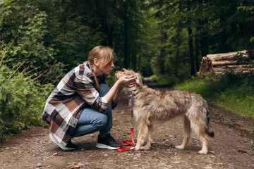 woman kneeling on a forest path, gently interacting with a dog, showcasing the bond of true...