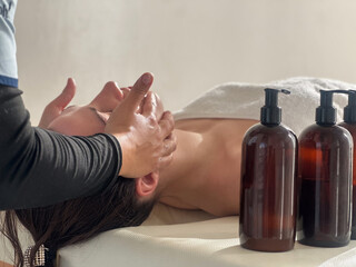 Young woman receiving a relaxing face  massage from a professional masseuse at a spa salon, lying...