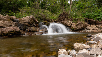 Mountain stream waterfall in Belianske Tatras, Slovakia. Scenic nature with rocks, clear water, forest background. Long exposure landscape perfect for travel and nature themes.