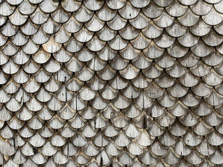 Abstract background with wooden scales. Close-up of an exterior wall covered with wooden shingles, resembling a traditional fish scale pattern. Architectural, historical, and rustic design concept.