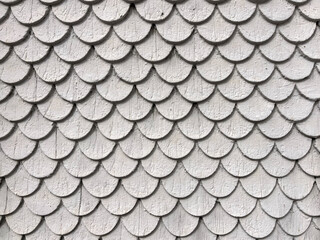 Abstract background with wooden scales. Close-up of an exterior wall covered with wooden shingles, resembling a traditional fish scale pattern. Architectural, historical, and rustic design concept.
