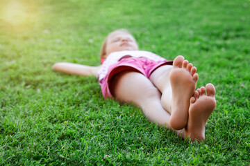 Holiday On Nature. Child Girl Lying down on Grass Barefoot with Sunlight. 