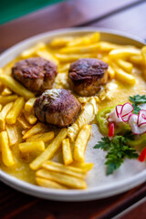 Juicy meatballs served with golden French fries on a white plate.