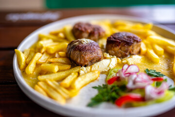 Juicy meatballs served with golden French fries on a white plate.