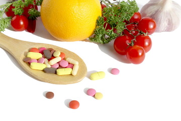 On a white background lies a wooden spoon with medicine and in the background are vegetables and fruits.