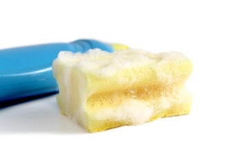 On a white background lies a sponge in foam and a bottle of dishwashing detergent.	