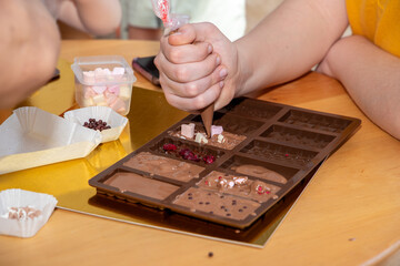 Children's master class on making chocolate, children make chocolate and chocolate candies. People pour melted white chocolate into silicone molds from a saucepan, close-up of their hands.
