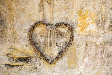 Wicker heart with ribbon hanging on aged stone wall. Rustic romance, handmade charm and countryside...