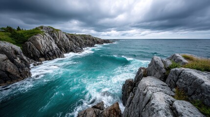 Obraz premium Rocky cliffs meet the turquoise ocean, with crashing waves revealing the power of nature. Clouds gather overhead, creating a moody atmosphere on the coastline.