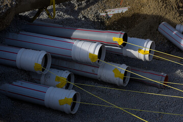 Several large, gray pipes with red stripes and yellow tape ends lie on a bed of gravel,...