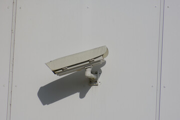 A subtle security camera casts a sharp shadow on a bright white wall, highlighting surveillance and...