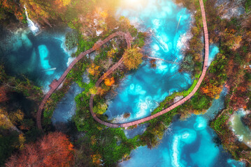 Aerial view of blue lakes in red autumn forest at sunrise. Morning in Plitvice Lakes park, Croatia. Colorful landscape with azure water, trees, wooden trails and bridges, orange foliage. Top view