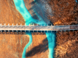 Aerial view of wooden bridge, azure river and orange grass at sunset in golden autumn. Zelenci lake, Slovenia, Triglav national park in fall. Top drone view of bridge, green water. Nature. Landscape