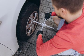 Close-up of a man changing a car tire in front of his house. The vehicle is lifted with a jack,...