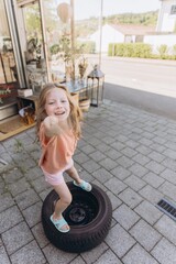 Child playing outside, balancing on a tire and holding a stick on a sunny day. Outdoor activity,...