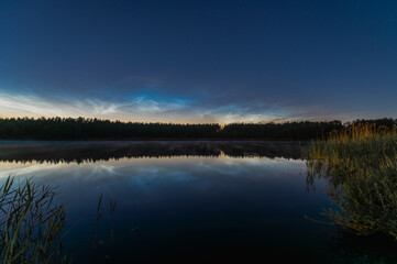 Noctilucent clouds over the forest lake in Latvia on June night