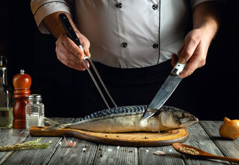 A chef is expertly filleting a mackerel on a wooden cutting board, using a knife and fork,...