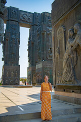 A girl in a yellow dress stands at the monument of the chronicles of Georgia
