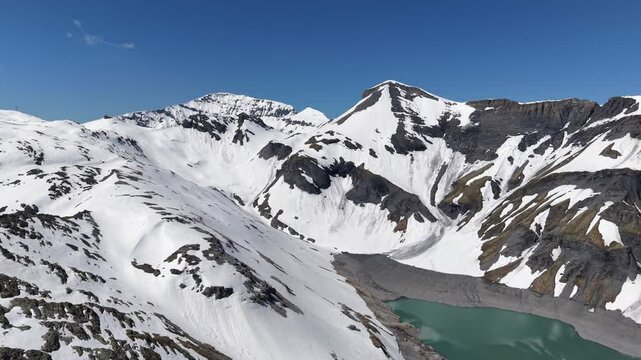 Vue a&eacute;rienne spectaculaire d&rsquo;un barrage en arc au c&oelig;ur des Alpes, entour&eacute; de neige et de montagnes rocheuses. Vid&eacute;o drone 4k 60fps