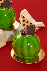 Delicious green pumpkin-shaped mousse cakes with mirror glaze on red background