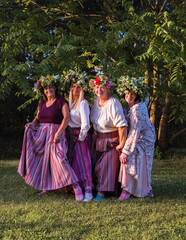 On the evening of the summer solstice, women show off their crowns on their heads and colorful, ornamented stockings on their feet. Outdoors in the park.