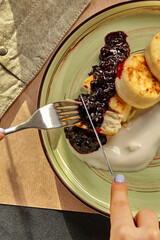 Woman eating cottage cheese pancakes with berry sauce and sour cream in restaurant