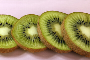 Sliced kiwi fruit arranged in a row. Each slice reveals vibrant green flesh and tiny black seeds....