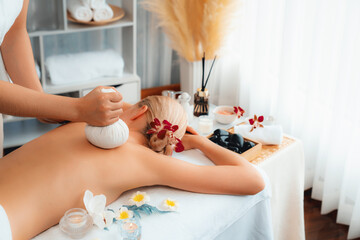 Hot herbal ball spa massage body treatment, masseur gently compresses herb bag on woman body....