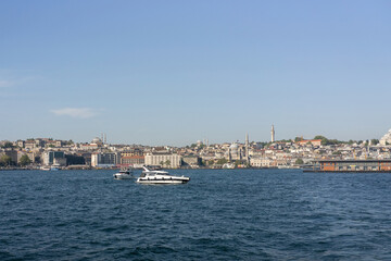 Fototapeta premium A wide view of the Bosphorus Strait in Istanbul, with the city's skyline and coastal buildings in the background. A ship sails across the calm waters under the clear blue sky
