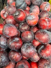 vibrant pile of dark red and purple plums with natural wax coating, displayed for sale.
