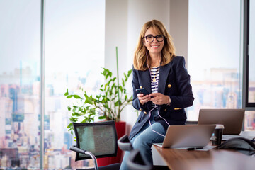 Blond haired business woman using a laptop and smart phone in a modern office