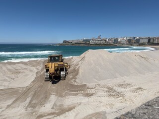 Bulldozer leveling sand on the beach, preparing it for summer season