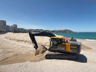 Excavator working on the beach, arranging the sand in front of the city skyline