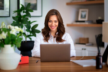 Middle aged woman sitting in her modern home and using laptop computer