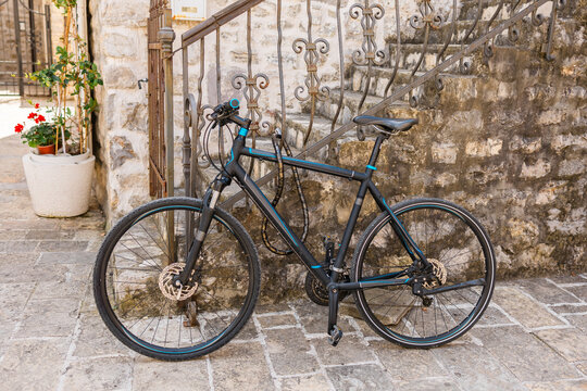 Modern black bicycle locked to wrought iron railing on stone street. Urban mobility, historical setting and travel lifestyle.