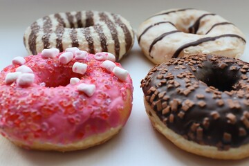 Top View of Four Colorful Donuts with Chocolate and Pink Glaze on White Surface – Confectionery Background