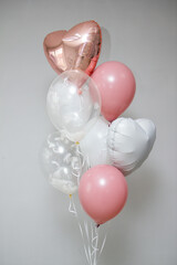 A bunch of elegant helium balloons in pink, white, and transparent colors with feathers and heart shapes, floating indoors against a light gray background. Perfect for celebrations or romantic themes.