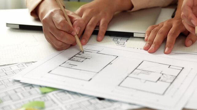 Professional engineer team discussion about house design on meeting table with architectural equipment and building blueprint scatter around at modern office. Focus on hand. Closeup. Delineation.