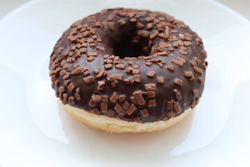 glazed doughnut, chocolate glaze and chocolate sprinkles, close up on white background 